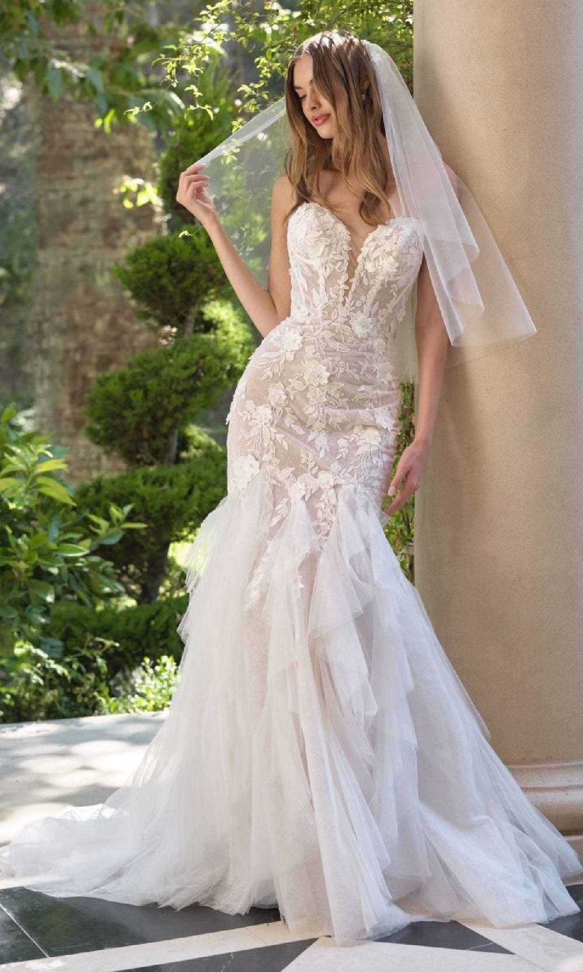 Woman in a white wedding dress with a veil standing outdoors.